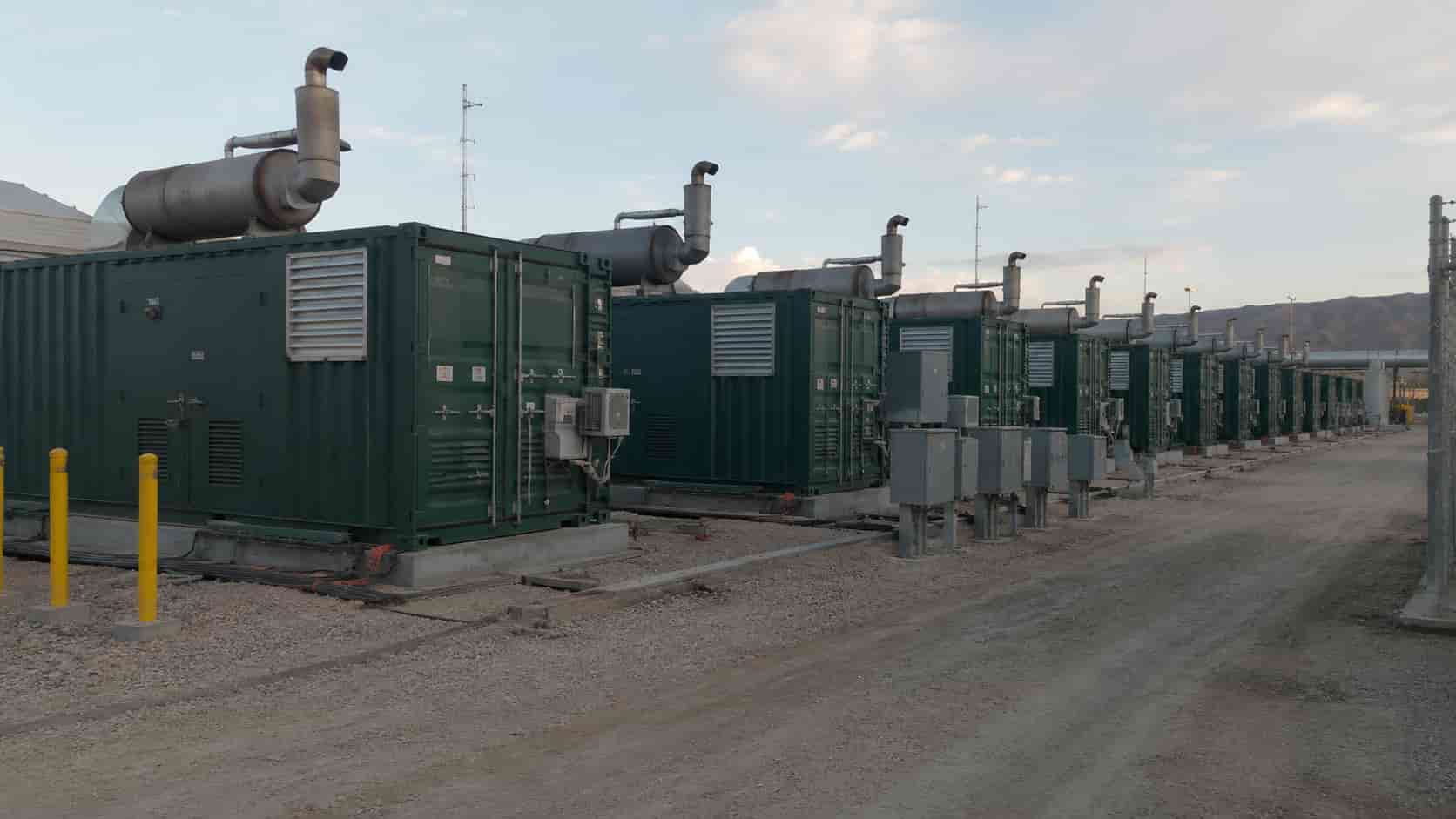 A row of 40ft containerized diesel generator sets installed at a remote industrial site, forming a modular power station with exhaust systems, switchgear, and power distribution equipment.