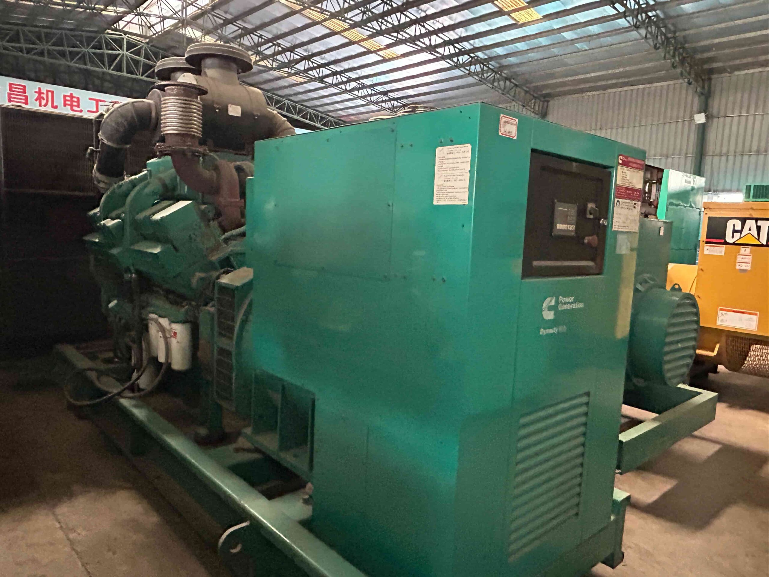 Used Cummins diesel generator set displayed in an industrial workshop, featuring an open-type engine, alternator, exhaust system, and heavy-duty base frame for commercial power applications.